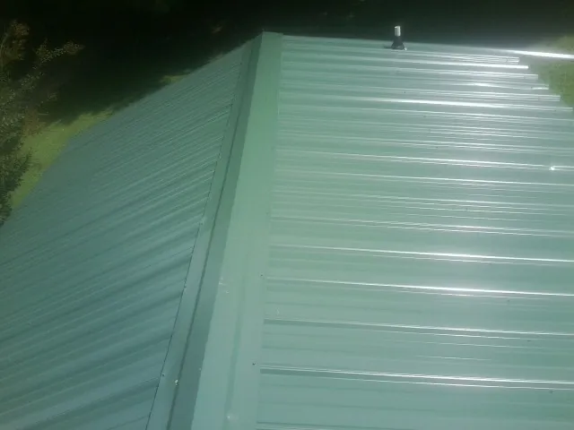 New green metal panels meeting at the ridge of a roof — Flat Roof Repair work by our crew in Adrian